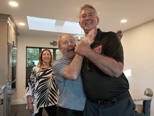 three people standing in kitchen with one man pretending to choke another man