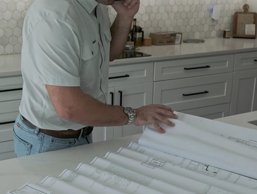 remodeler in kitchen looking over plans on the counter while on the phone