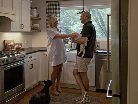 man and woman standing in the kitchen smiling with two dogs