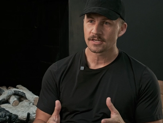 man with black shirt and black hat sitting in front of a black fireplace