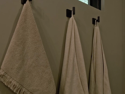 three neutral colored towels hanging on black hooks